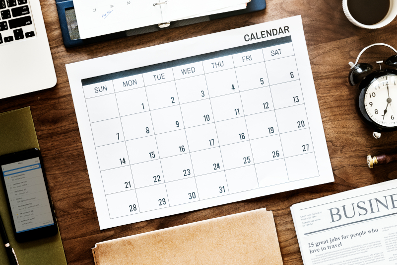 Calendar on desk surrounded by newspaper, laptop, clocks, organizer Calendar on desk surrounded by newspaper, laptop, clocks, organizer